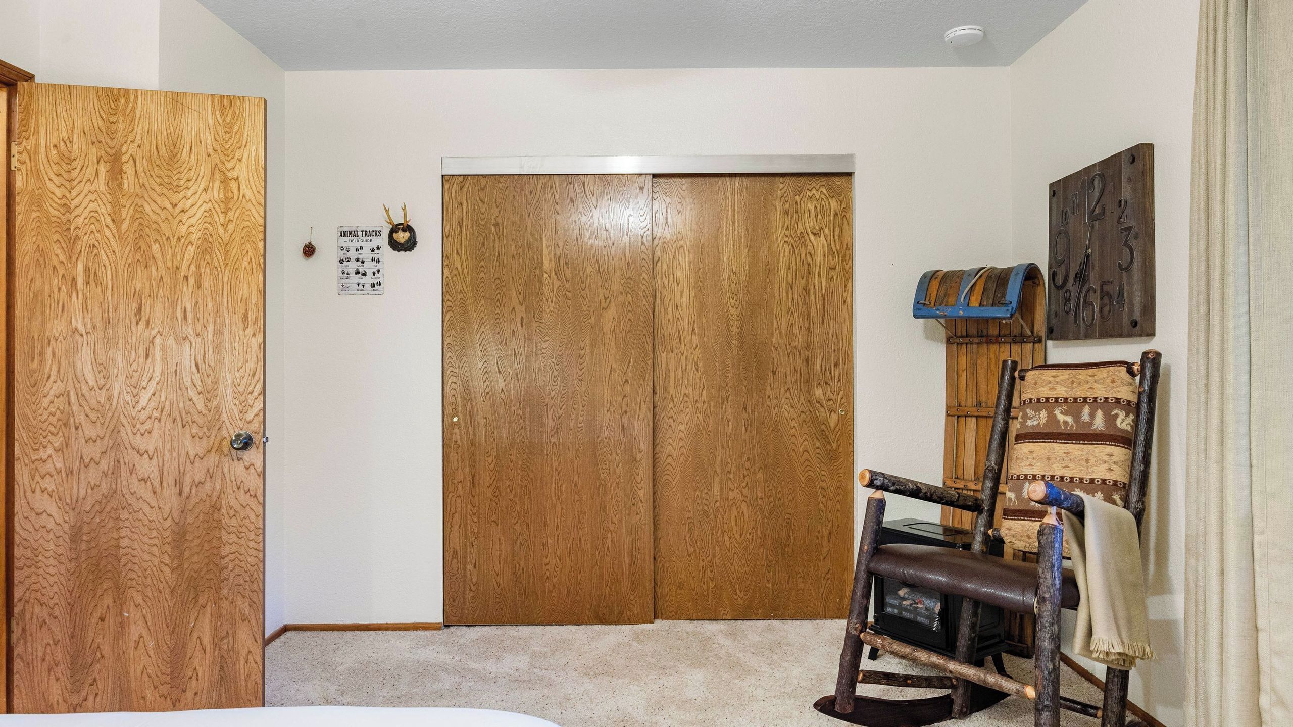 A room with a wooden wardrobe, a chair with a blanket, a wall clock, and a fireplace.