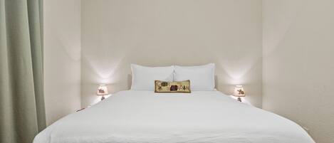 A bed with white bedding, two bedside lamps, and a decorative pillow with a cabin design.
