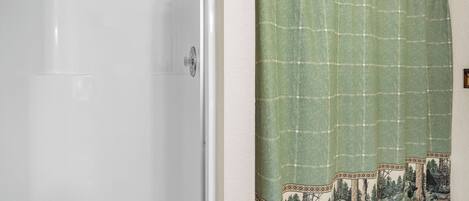 A bathroom with a bathtub, a shower, and a curtain with a forest pattern.