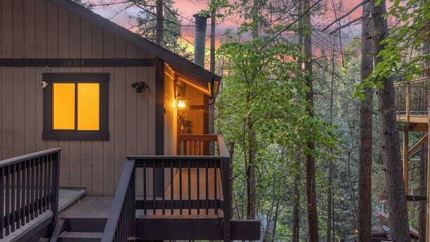 Una cabaña con fachada de madera, un balcón y una ventana con luz cálida.
