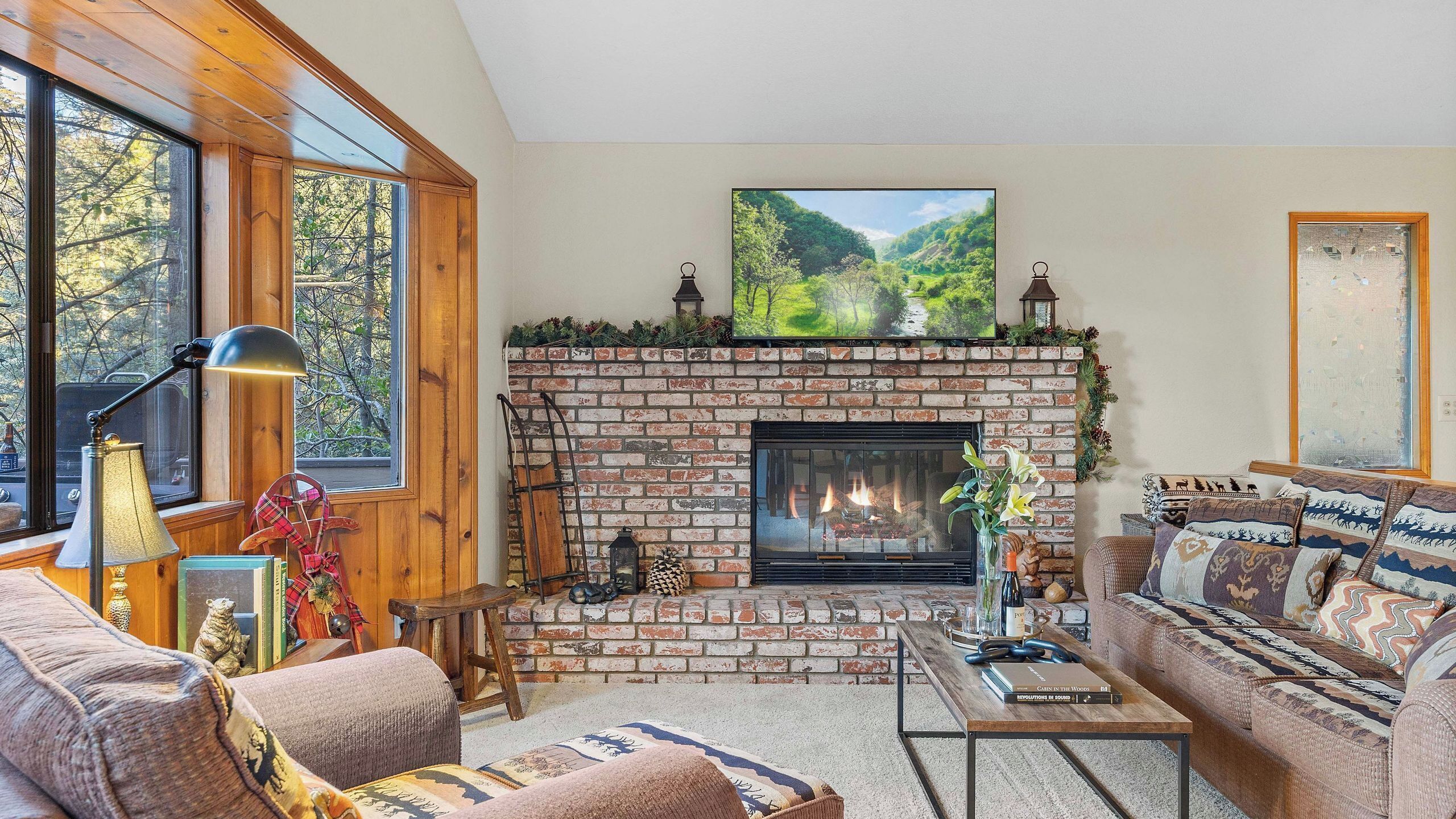 A cozy living room with a fireplace, wooden walls, and a large window.