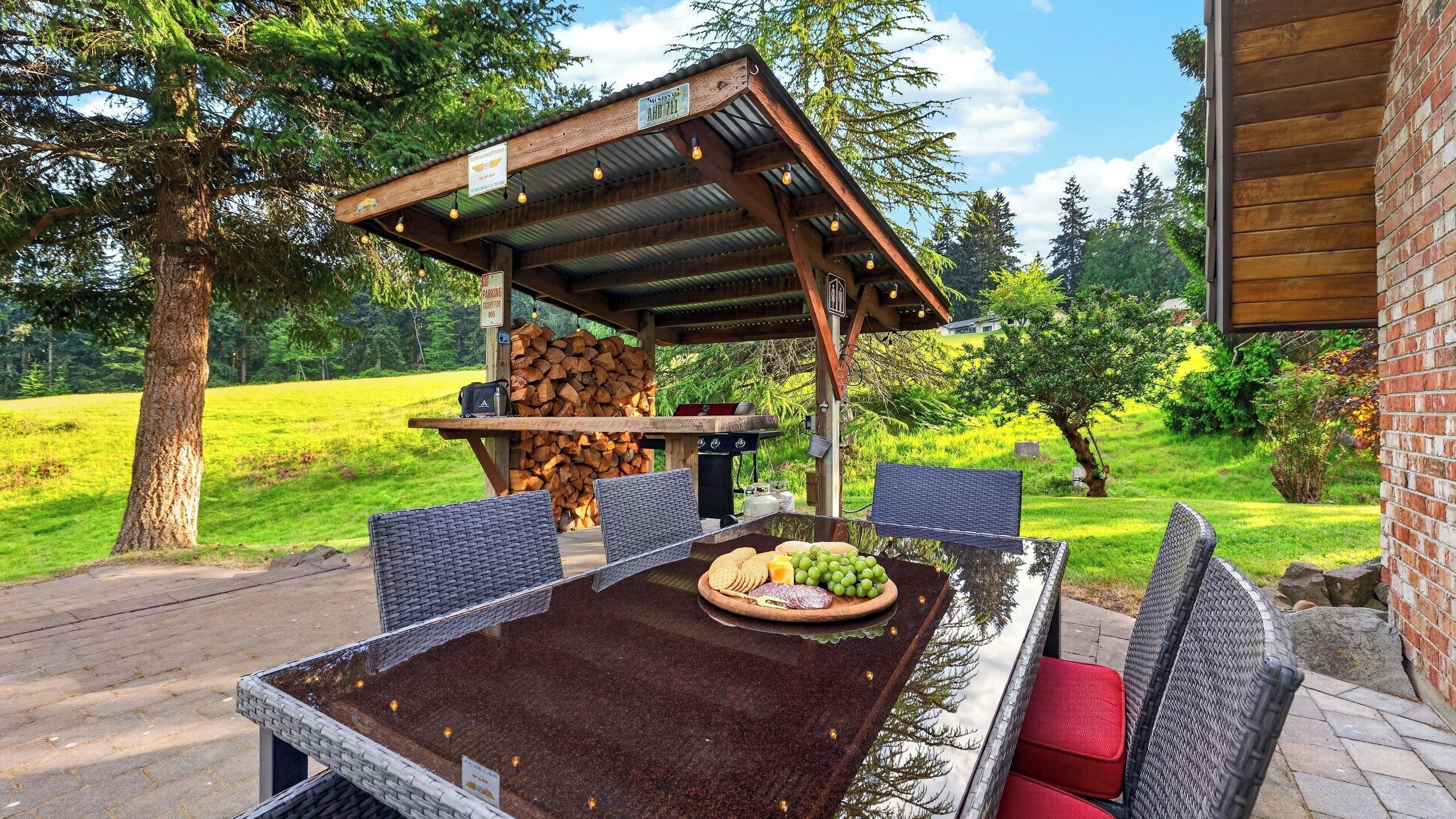 An outdoor dining area with a covered table, chairs, and a grill.