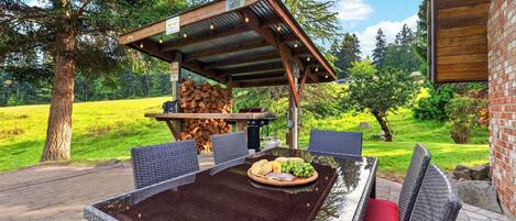An outdoor dining area with a covered table, chairs, and a grill.