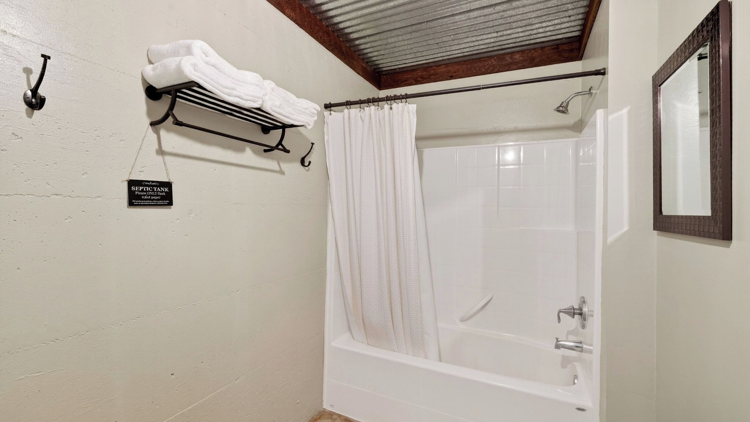 A bathroom with a bathtub, a shower curtain, a towel rack, and a sign indicating the use of a septic tank.