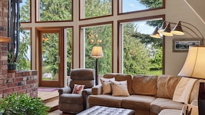 Ein geräumiges Wohnzimmer mit großen Fenstern, einem Ledersofa, einem Sessel und einer Lampe.