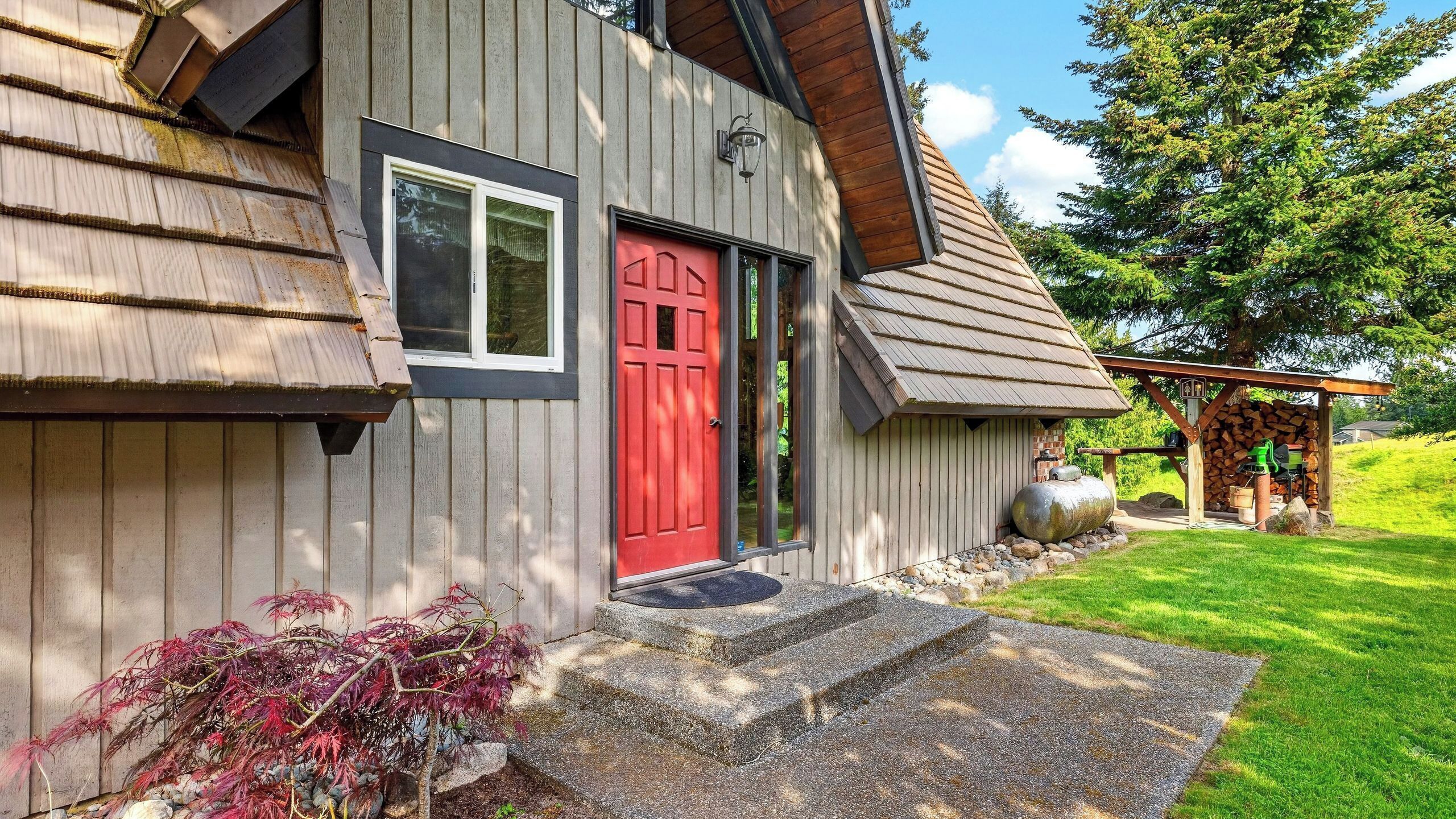 A wooden house with a red door, a front porch, and a small outdoor area with a grill.