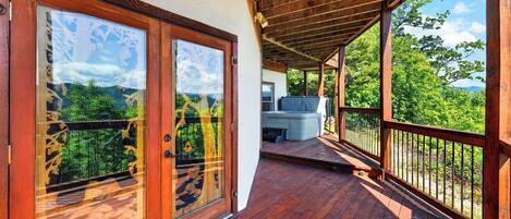 Une terrasse en bois avec une porte vitrée donnant sur une pièce, un barbecue et une vue sur la verdure.