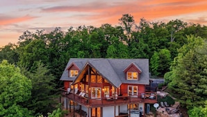A two-story wooden house with a balcony, surrounded by dense forest. - Serenity Ridge by Avantstay Spa + Game Room + Firepit Deck + Mountain Views Short Drive to Pigeon Forge (Sevierville)
