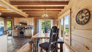 Ein Holzblockhaus-Interieur mit Küche, Essbereich und einem großen Fenster mit Blick ins Freie.