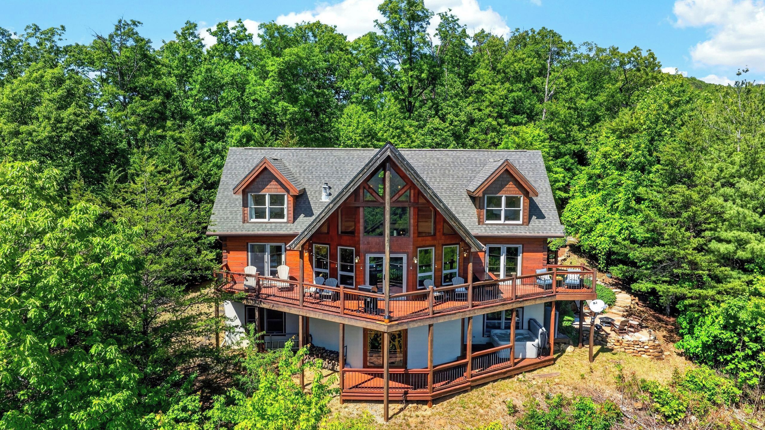 Une cabane en rondins à deux étages, dotée d’une terrasse périphérique, et entourée d’une forêt dense.