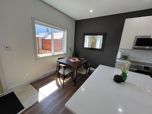 A modern kitchen with a dining area, a large window, and a view of a backyard.