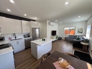 A modern kitchen with white cabinets, a stainless steel refrigerator, and a dining area with a wooden table.