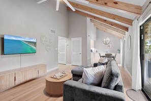 Ein modernes Wohnzimmer mit großem Fernseher, Holzbalkendecke, einem grauen Sofa und einem runden Couchtisch.