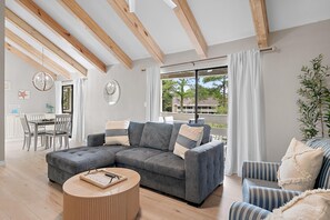 Ein modernes Wohnzimmer mit einer Eckcouch, einem runden Couchtisch und einem Essbereich mit weißem Tisch und Stühlen.
