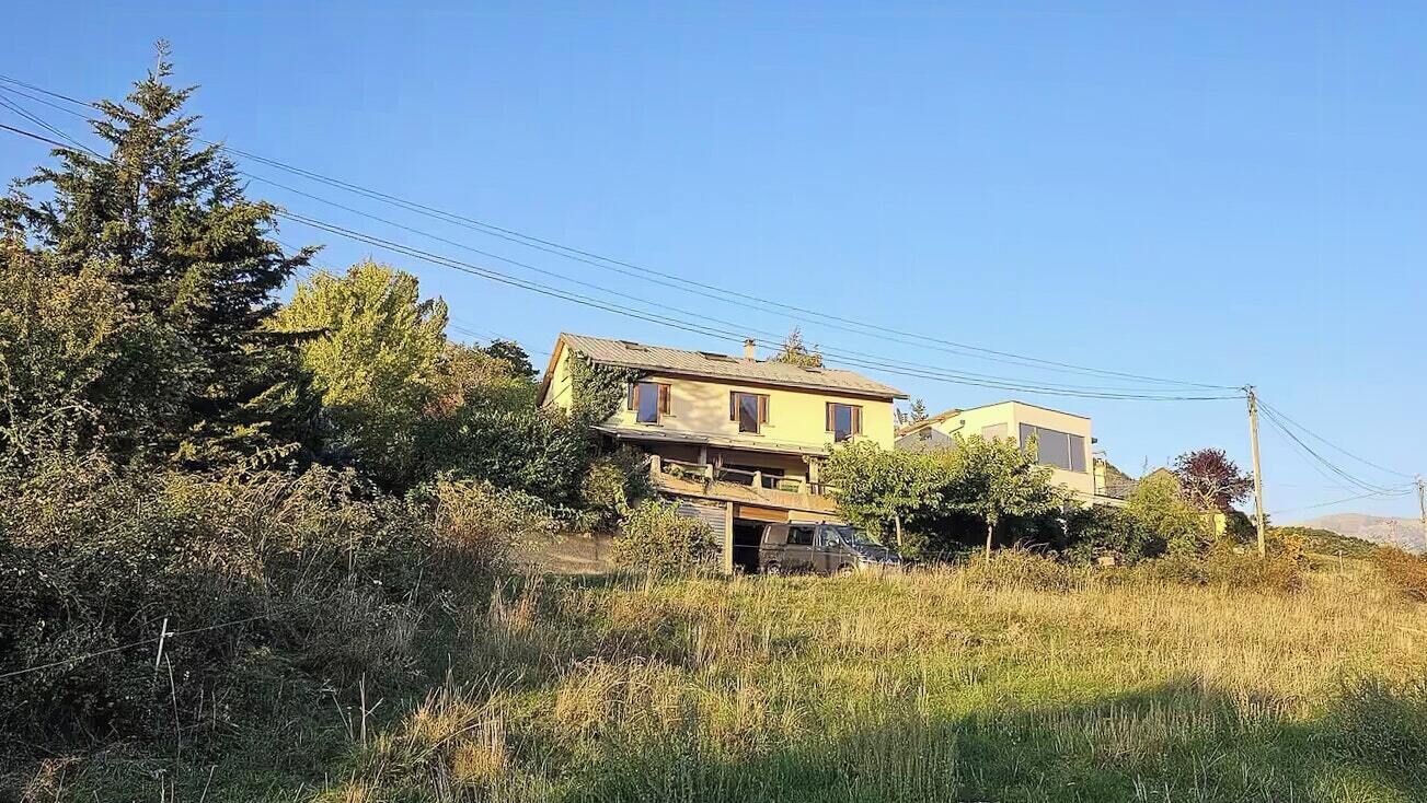 A two-story house with a sloped roof, surrounded by trees and vegetation.