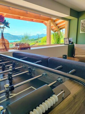 Ein Zimmer mit Fußballtisch, Sofa, Blumenvase und Bergblick durch ein Fenster.