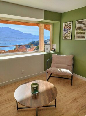 Ein Zimmer mit Blick auf ein Gewässer und Berge, ein Sessel, ein kleiner Tisch mit Kerze und Kunstwerke an der Wand.