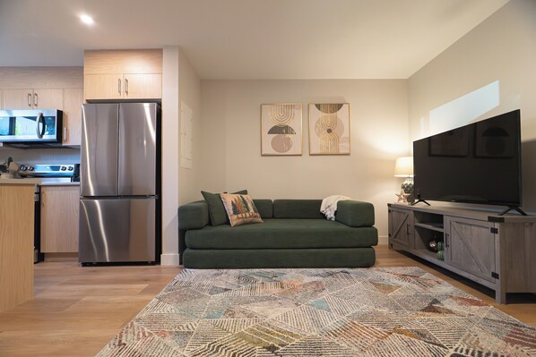 Un espacio habitable compacto con kitchenette, un sofá, televisor de pantalla plana y obras de arte en las paredes.