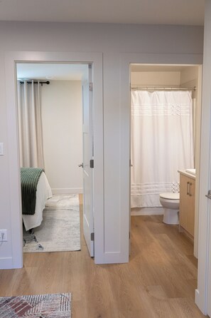 Un pasillo que conduce a un dormitorio con cama y un baño con inodoro y cortina de ducha.