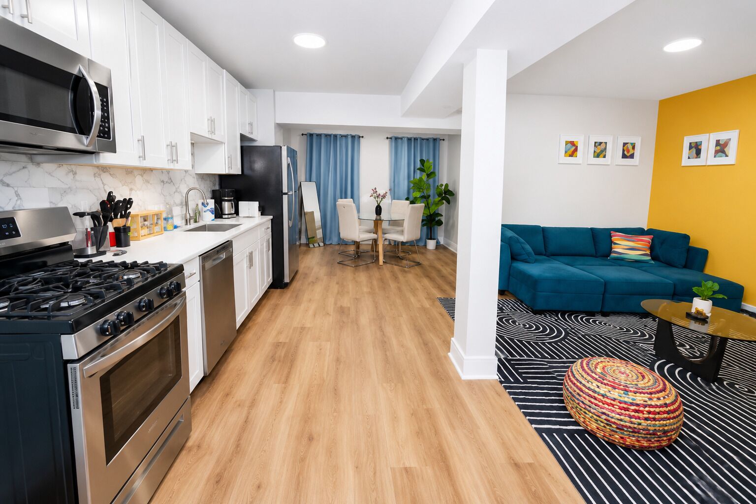 Una cocina moderna con estufa, microondas y refrigerador, un comedor con mesa y sillas, y una sala de estar con sofá y mesa de centro.