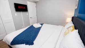 A neatly made bed with a blue throw, white bedding, and a TV displaying 'NETFLIX' on the wall. - Chicago Edgewater 3BR - 9 Min Walk to Loyola (Chicago)