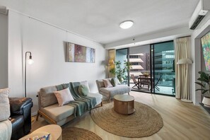 Ein modernes Wohnzimmer mit Sofa, Sessel, rundem Couchtisch und einem großen Fenster mit Blick auf Gebäude.