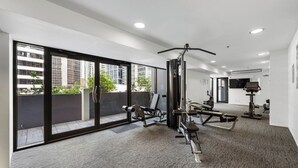 Une salle de sport équipée de matériel d’exercice, dotée de grandes fenêtres et offrant une vue sur les bâtiments.
