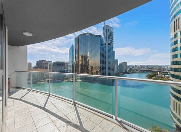 Ein Balkon mit Glasgeländer, der auf einen Fluss und eine Stadtansicht blickt.