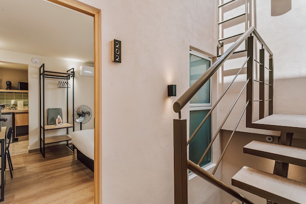 Una habitación con cama, escritorio, silla, ventilador, ventana y escalera.