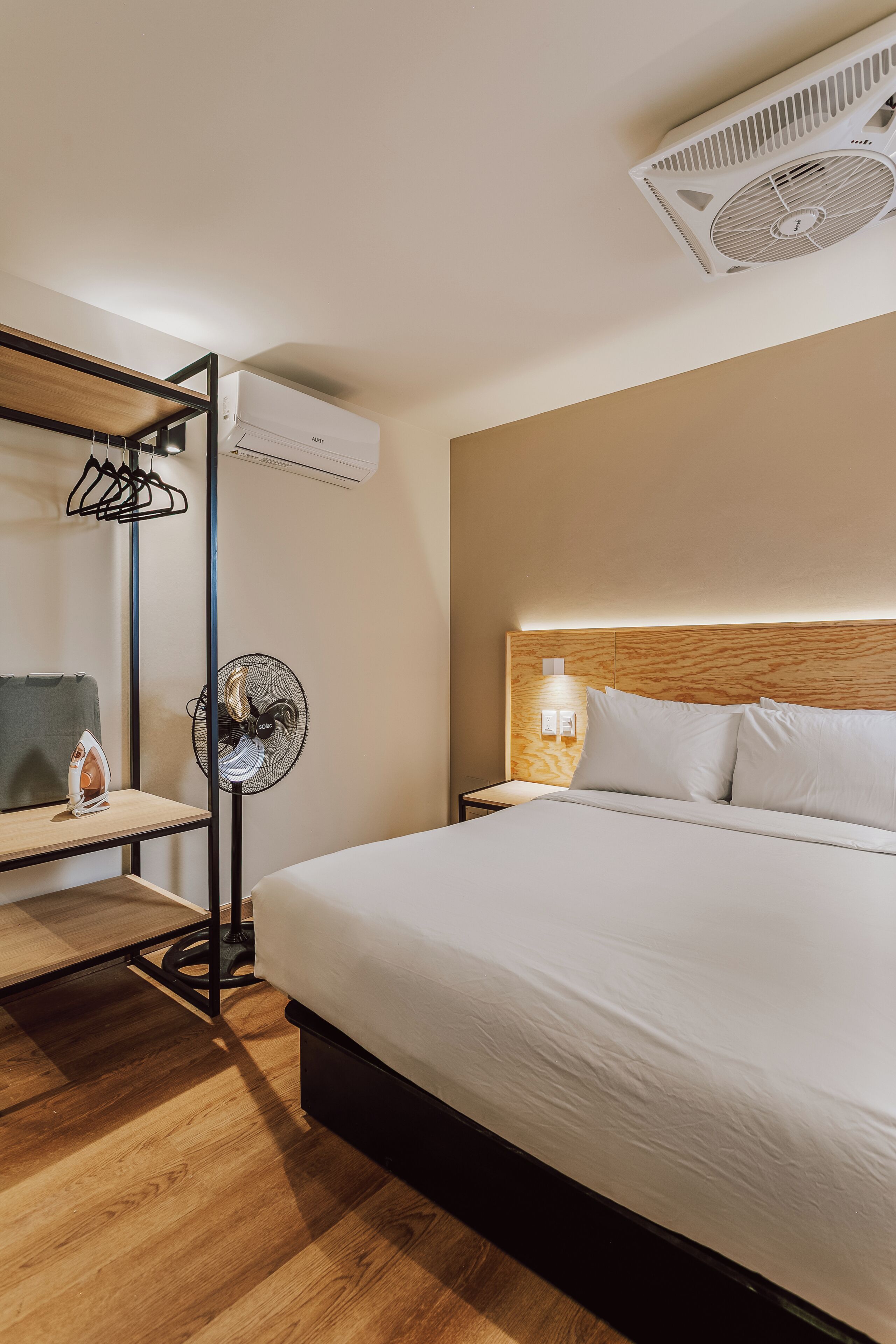 Une chambre d’hôtel équipée d’un lit, d’une planche à repasser, d’un ventilateur et d’un appareil de climatisation.