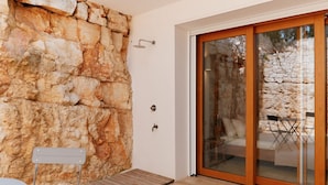 A modern room with a stone wall, a sliding glass door, a small table, and a bench. - Villa Aurora - Ostuni (Ostuni)