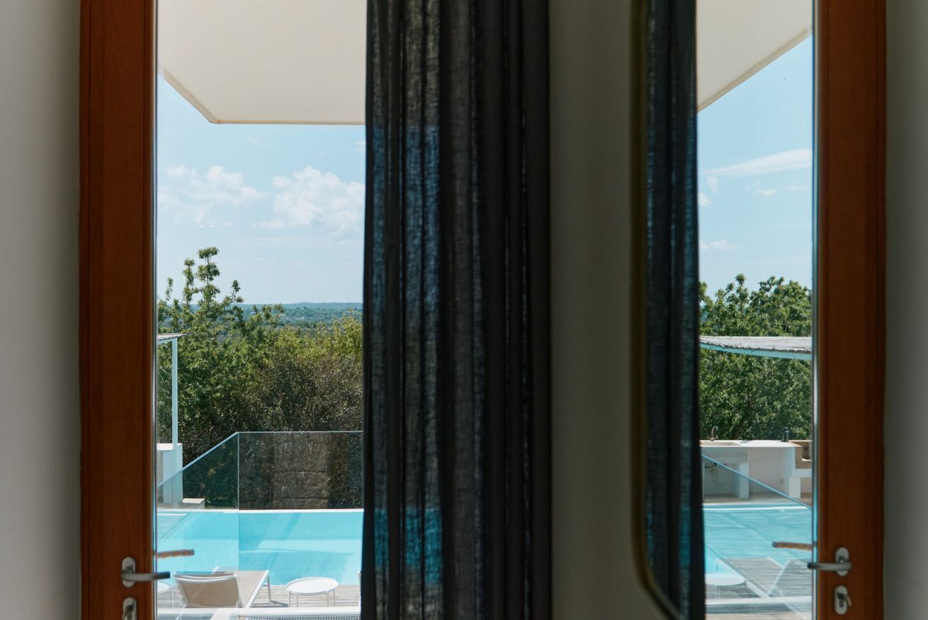 Blick durch eine Tür auf einen Poolbereich mit blauem Himmel und viel Grün.