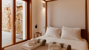 A hotel room with a large bed, a bedside table, a lamp, and a view of a stone wall through a glass door. - Villa Aurora - Ostuni (Ostuni)