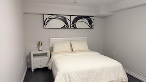 Ein Schlafzimmer mit einem weißen Bett, einem Nachttisch mit Lampe und einem Gemälde über dem Bett.