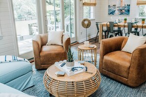 A cozy living room with two brown leather sofas, a round wicker coffee table, and a dining area with a wooden table and chairs.