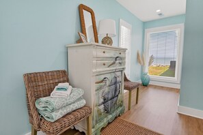 Ein Zimmer mit einem Korbstuhl, einem Schminktisch mit Vogelgemälden und Blick durch ein Fenster.