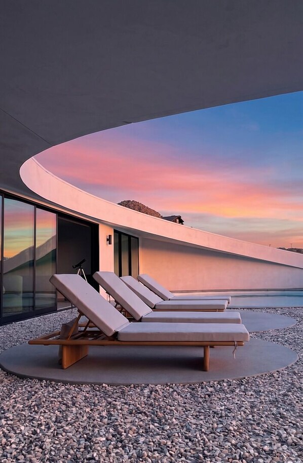 Ein stilvoller Lounge-Bereich mit Liegestühlen, einer gewölbten Wand und Blick auf den Sonnenuntergang.