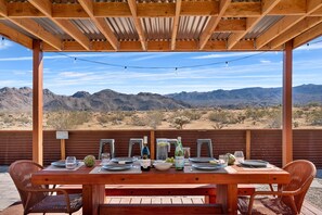 Una pérgola de madera con una mesa lista para comer, con vistas a un paisaje desértico.