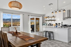 A modern kitchen with a large island, white cabinetry, and a view of the desert landscape. - Relaxing Desert Oasis · Hot Tub · Private Pool · 10 mins from National Park (Joshua Tree)