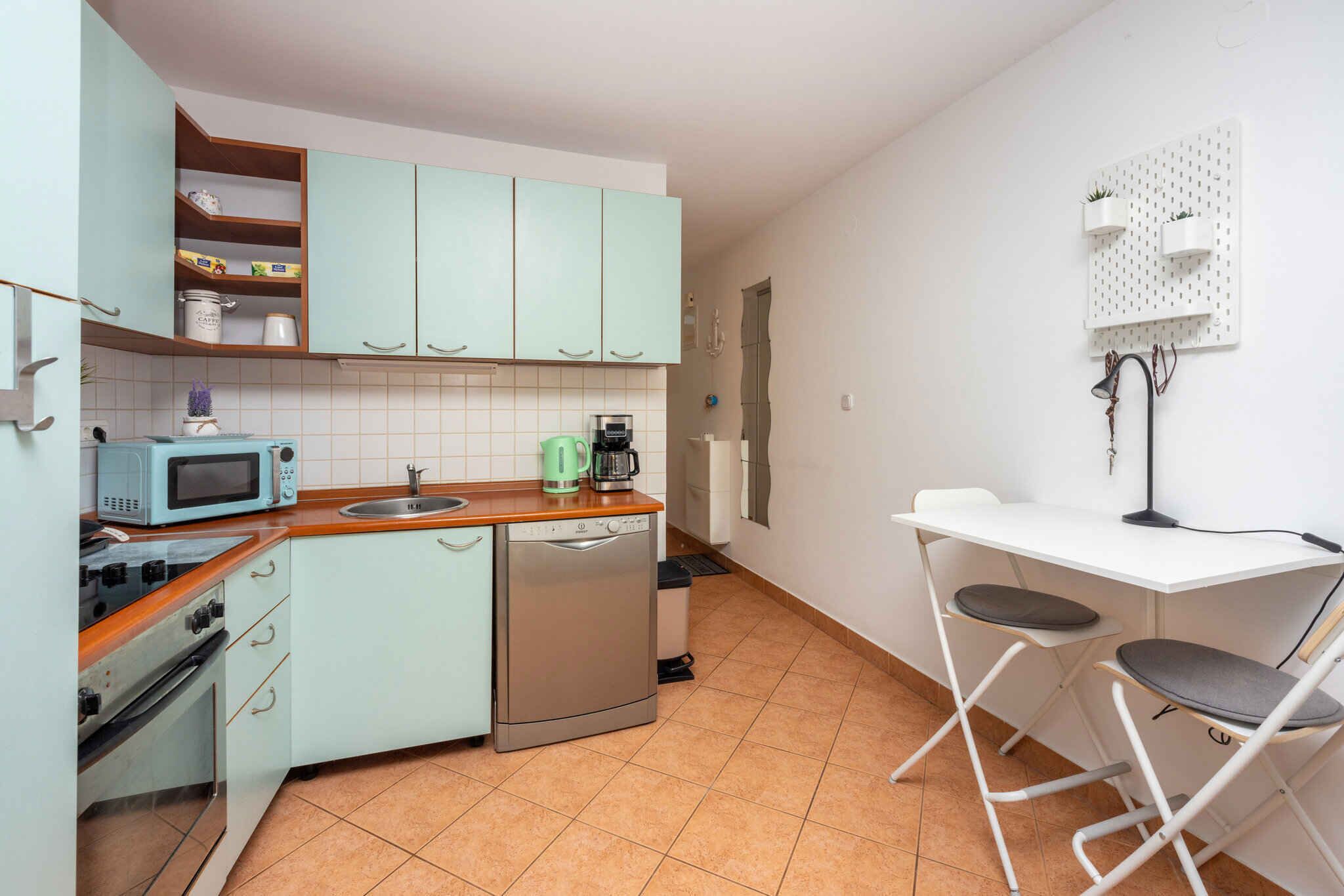 A compact kitchen with a microwave, coffee maker, and dishwasher. There is a small dining area with a white table and two chairs.