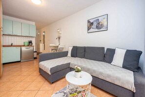 Ein modernes Wohnzimmer mit einer grauen Eckcouch, einem weißen Couchtisch und einer Küchenzeile mit hellgrünen Schränken.