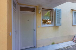 Ein Gebäude mit einer geschlossenen Tür, einem Fenster mit Rollläden und einem kleinen Außenbereich mit einem Fahrrad.