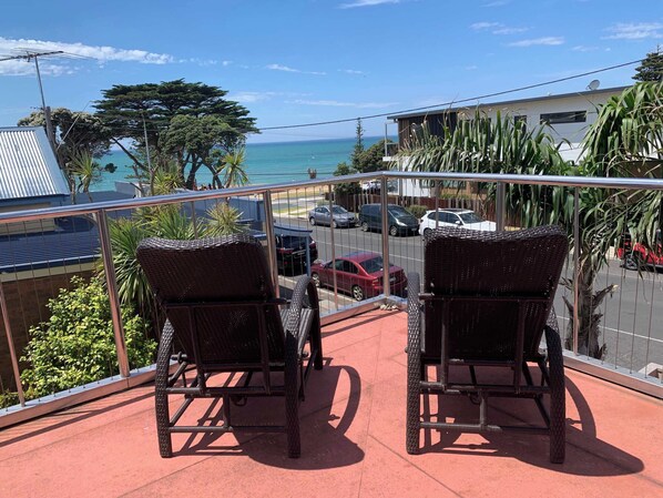 Un balcon avec deux fauteuils en osier, une vue sur la mer et des voitures garées.