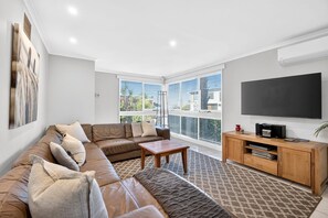 A living room with a sofa, coffee table, TV, and entertainment unit. - Sea View Steps to Central Esplanade Pet Friendly (Torquay)
