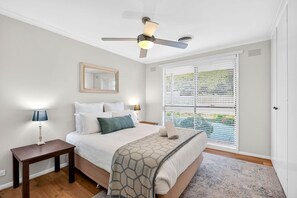 A bedroom with a bed, bedside tables, a ceiling fan, a window with blinds, and a door. - Sea View Steps to Central Esplanade Pet Friendly (Torquay)