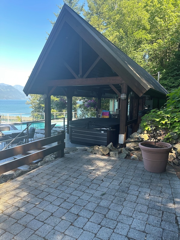 A covered outdoor seating area with a view of the sea, a pool, and a mountainous landscape.