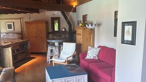 A cozy living room with a wooden ceiling, a red sofa, a white armchair, and a blue coffee table.
