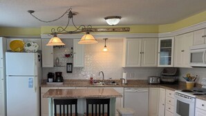 A kitchen with white cabinets, a granite countertop, a refrigerator, a dishwasher, a stove, and a dining area with yellow chairs. - Perfect Norris Lake 2Br condo in Deerfield Resort with amazing lake views! (LaFollette)