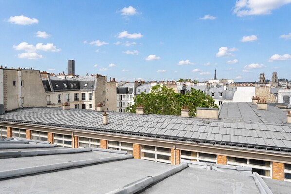 A rooftop terrace with a view of surrounding buildings, including a church spire. - Panorama of the Paris Rooftops - Welkeys (Paris)