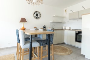 A modern kitchen with a wooden table, chairs, a clock, and basic appliances. - The Balcony of the Port in Capbreton - Welkeys (Capbreton)